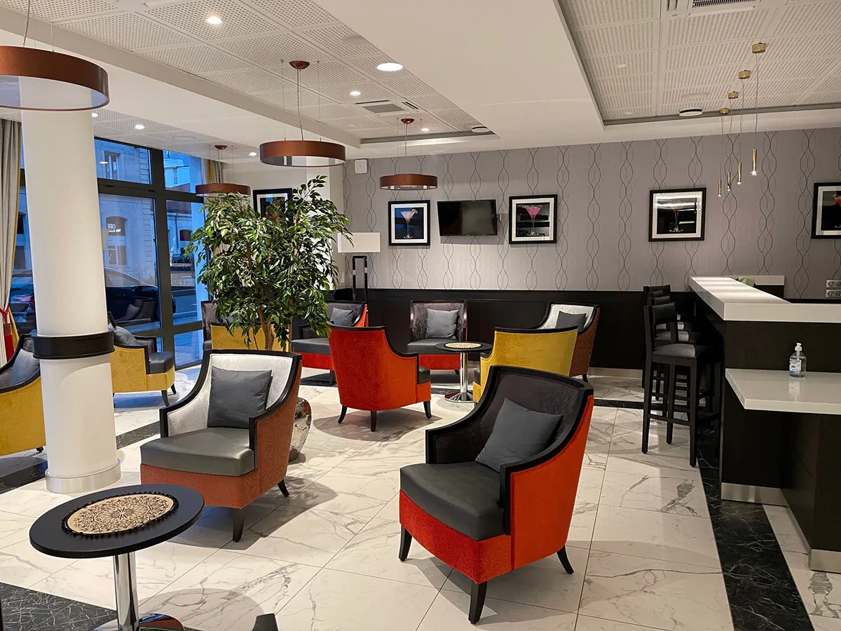 Lounge bar of the OBEO senior residence in Aix-les-Bains, with red and yellow armchairs, a bar counter, marble flooring and copper pendant lights