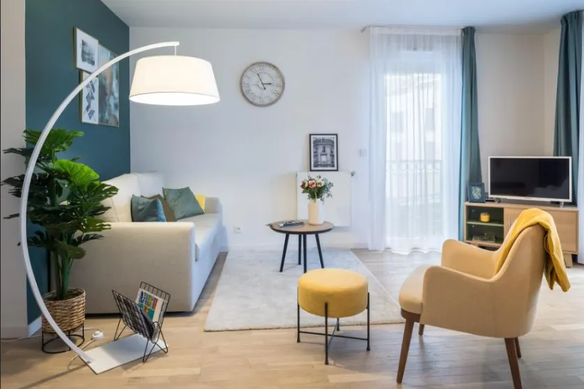 Furnished living room in an OBEO apartment: pale sofa, yellow armchair, plants and an arc lamp