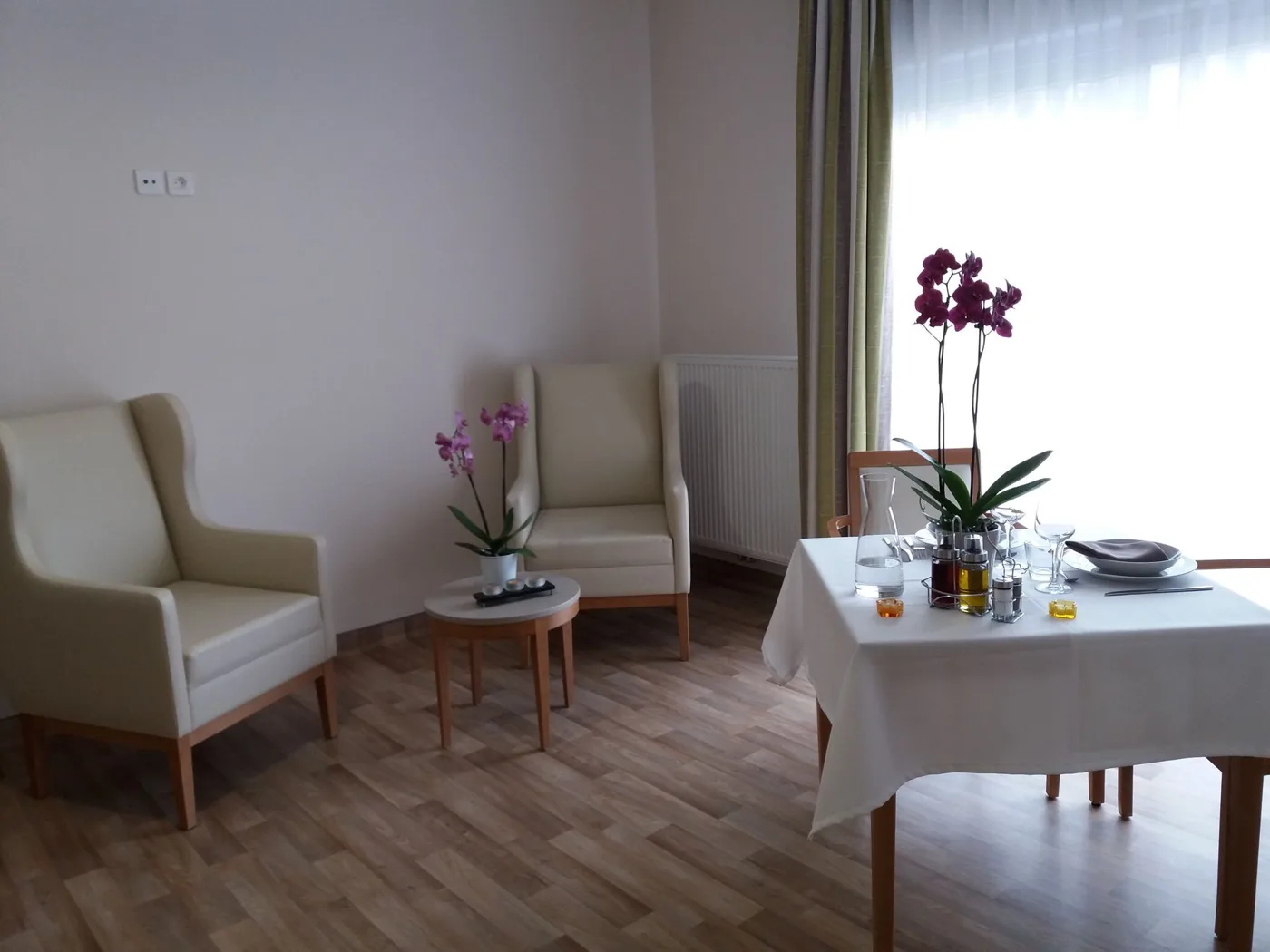 Coin salon d’un logement du Cheylard : deux fauteuils à oreilles, table basse et table dressée près de la fenêtre, orchidées en fleurs