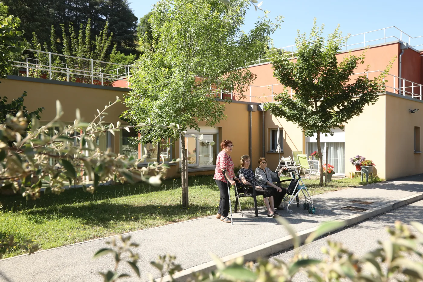 Residents sitting outdoors around a table among the trees, in front of the residence
