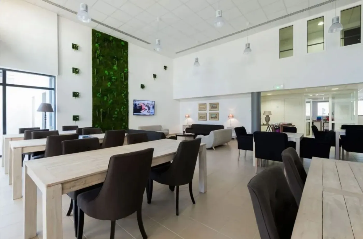 Bright lounge and dining room at the OBEO senior living residence in Nevers, with a living green wall, large light-wood dining tables and a cosy seating area