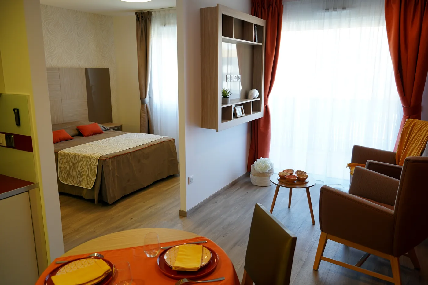 A furnished studio with double bed, red curtains and an armchair by the window