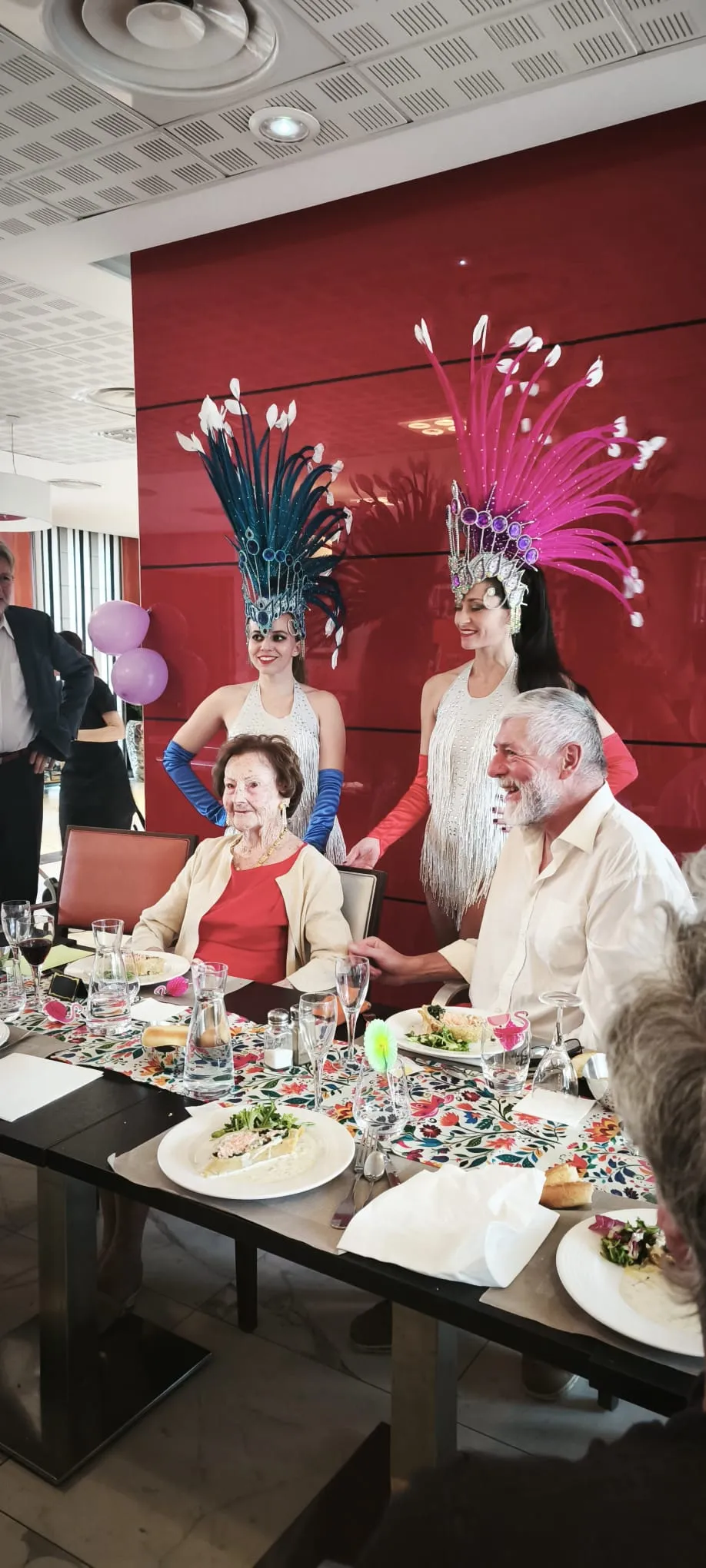 The guest of honour surrounded by cabaret dancers in feathered headdresses at the laid birthday table
