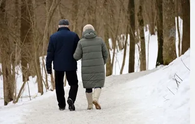Un couple de personnes âgées en manteaux d'hiver s'éloigne sur un chemin enneigé bordé d'arbres nus