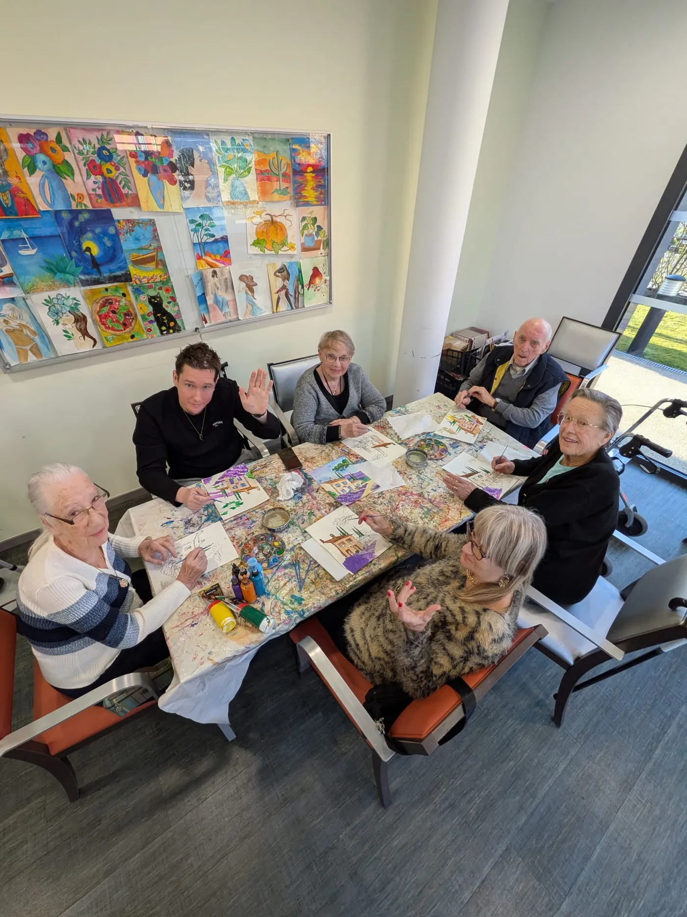 Residents and a young volunteer working together on colourful collages, children's drawings pinned on the wall behind