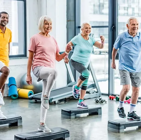 A group of seniors following a step class in a bright gym, each lifting one knee in time with the coach