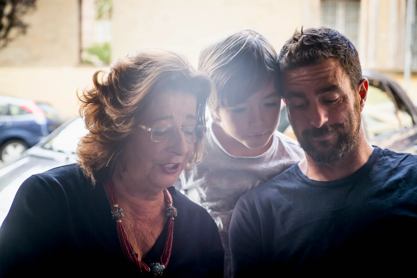 A grandmother, a teenage girl and a younger man leaning in close together outdoors