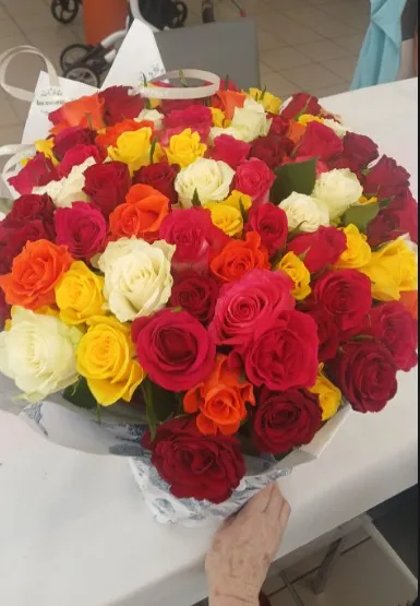 Un gros bouquet de roses rouges, jaunes, orange et blanches posé sur une table