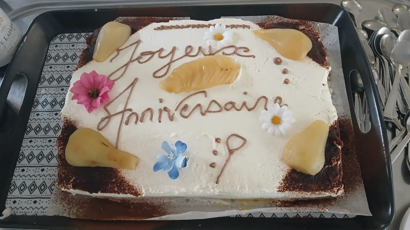 A cream-iced birthday cake decorated with pear slices and flowers, Happy Birthday piped in chocolate in French