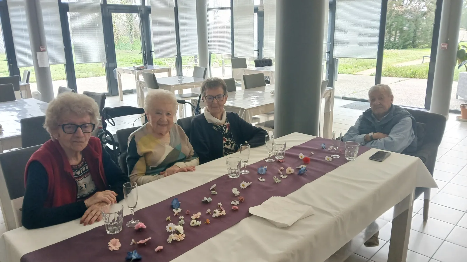 Four residents sitting together at the confetti-strewn table, waiting for the birthday tea to begin