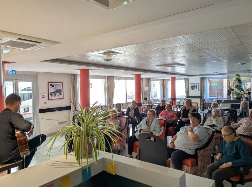 The lounge full of residents gathered around the musician and his guitar