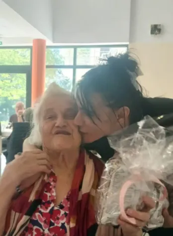 A member of staff leaning down to kiss a resident on the cheek as she holds her wrapped present