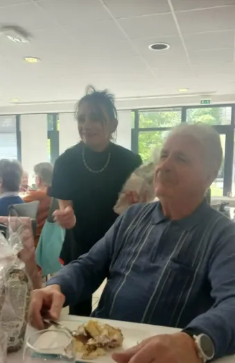 A resident enjoying a slice of cake while a staff member stands beside him