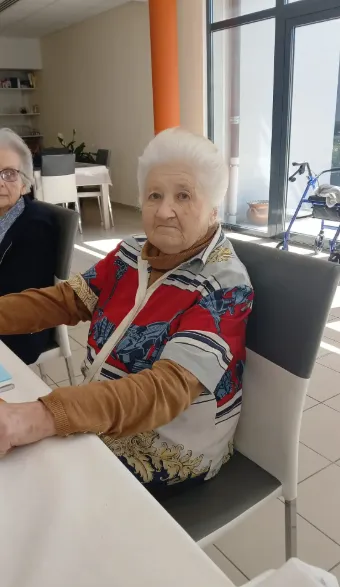 A white-haired resident smiling at the table in her red patterned jacket