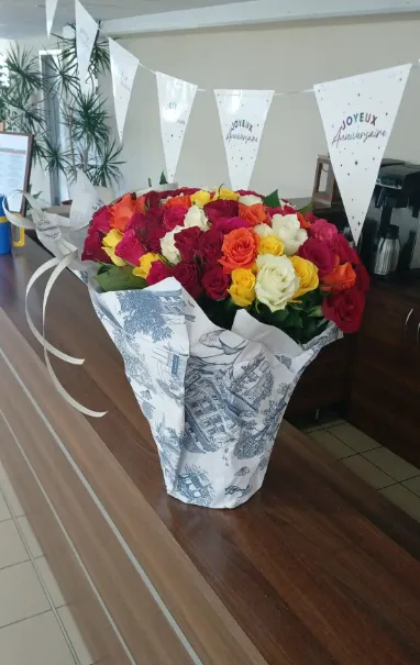 A bouquet of multicoloured roses on the sideboard beneath Happy Birthday bunting in French