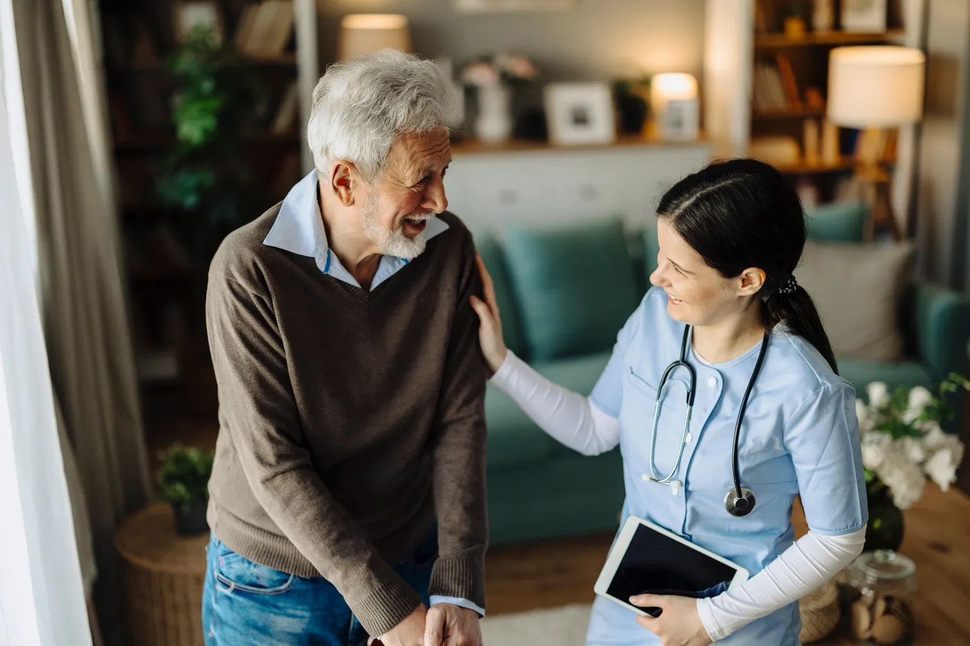 An older man walking arm in arm with a nurse who is carrying a notebook