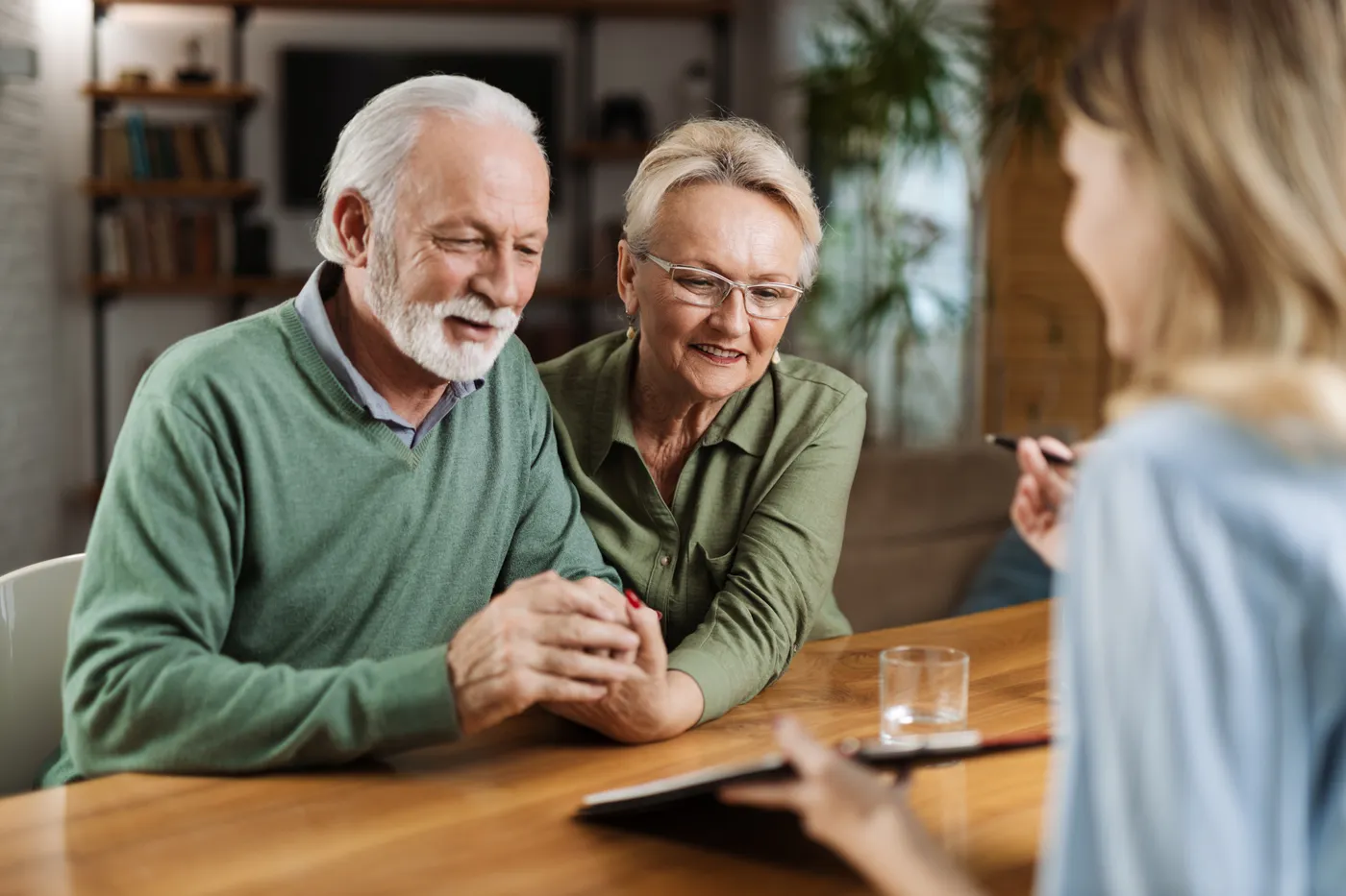 Un couple de seniors main dans la main face à une conseillère qui prend des notes