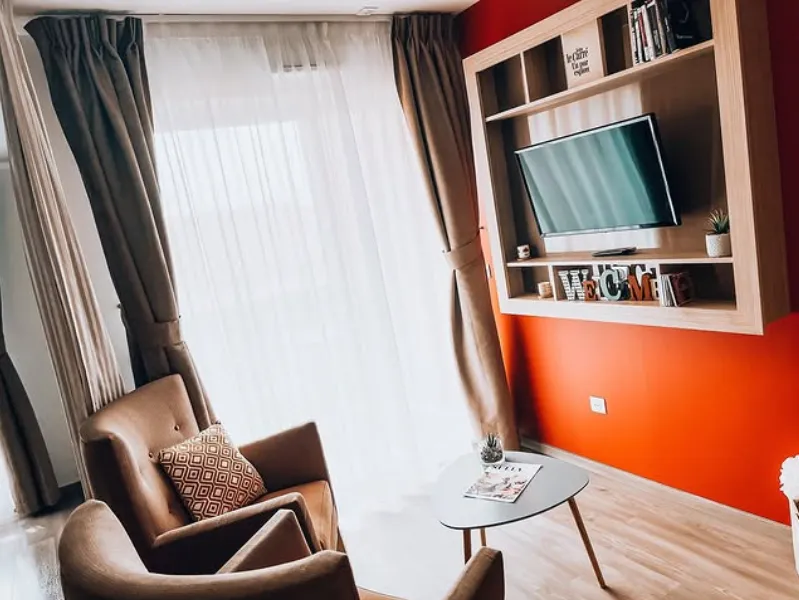 Un coin salon avec fauteuils, table basse et téléviseur encastré dans un mur orange
