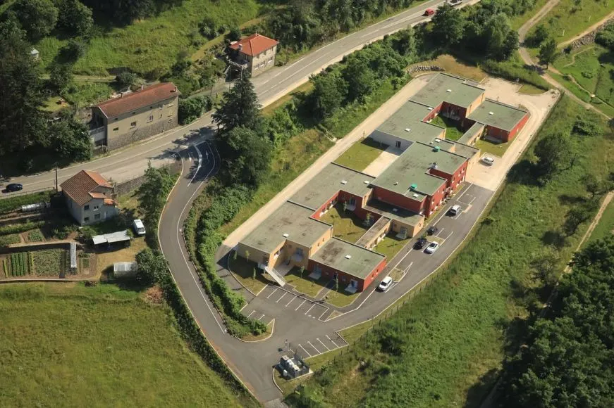 Vue aérienne de la résidence du Cheylard et de son parking, nichés dans la vallée boisée
