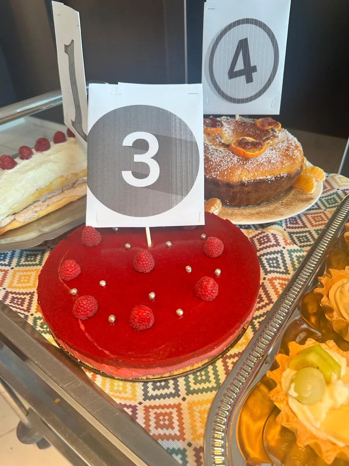 Les gâteaux du concours alignés avec leurs numéros, dont un entremets rouge aux framboises