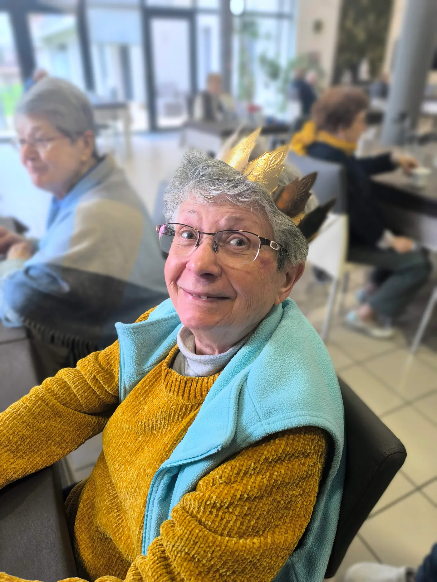 Couronne dorée sur la tête, une personne résidente se retourne en souriant vers l'objectif pendant le goûter