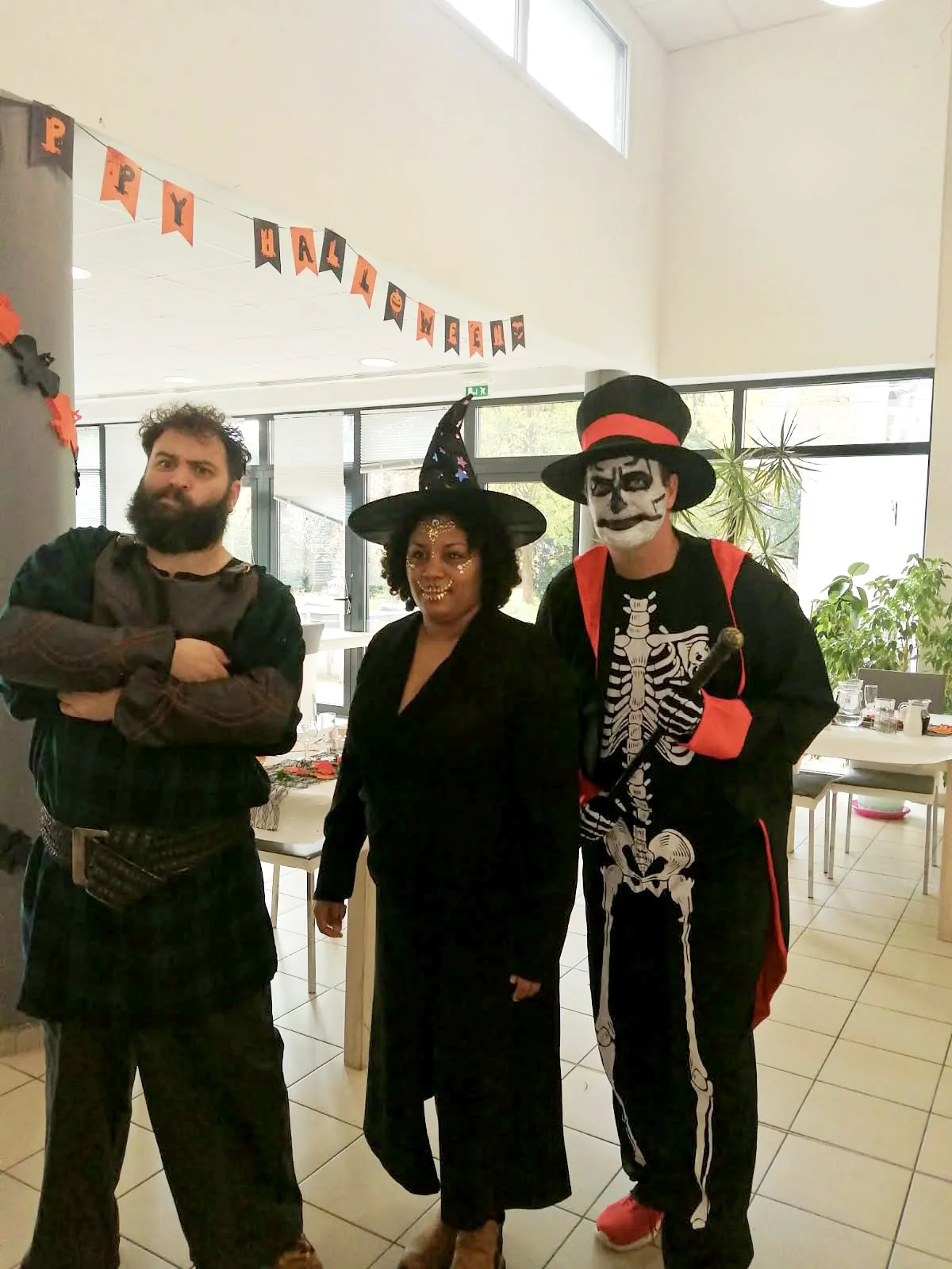 Trois membres de l'équipe déguisés pour Halloween, dont une sorcière et un squelette, dans le hall décoré