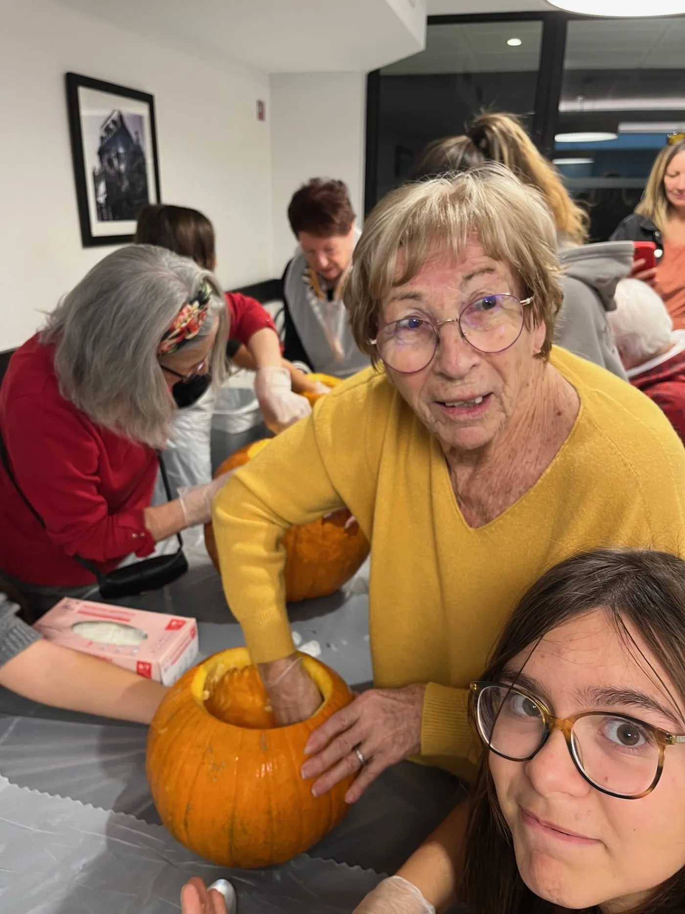 A resident and a teenage helper working on a pumpkin, others carving behind them