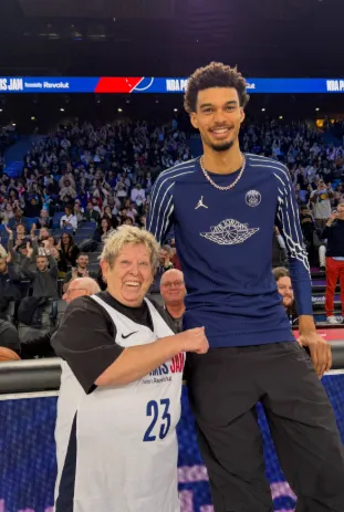 A senior fan posing courtside with a tall professional basketball player
