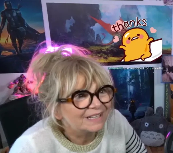 An older woman in red glasses live-streaming a video game, a thanks overlay on the screen behind her