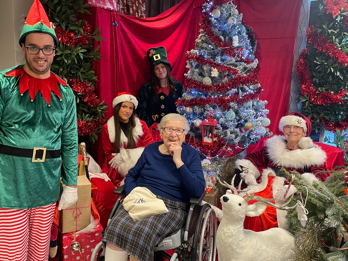 Staff dressed as elves and Father Christmas posing with residents beside the decorated tree