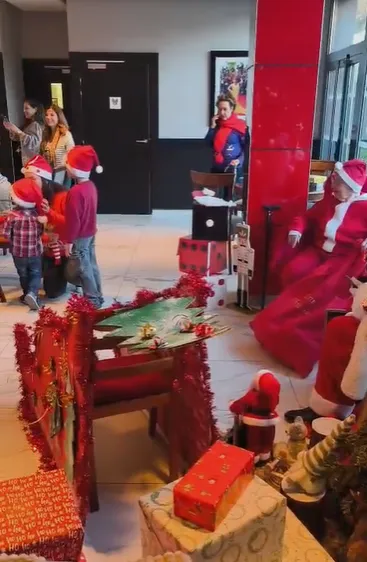 Des enfants s'avancent vers le Père Noël près de la table drapée de rouge