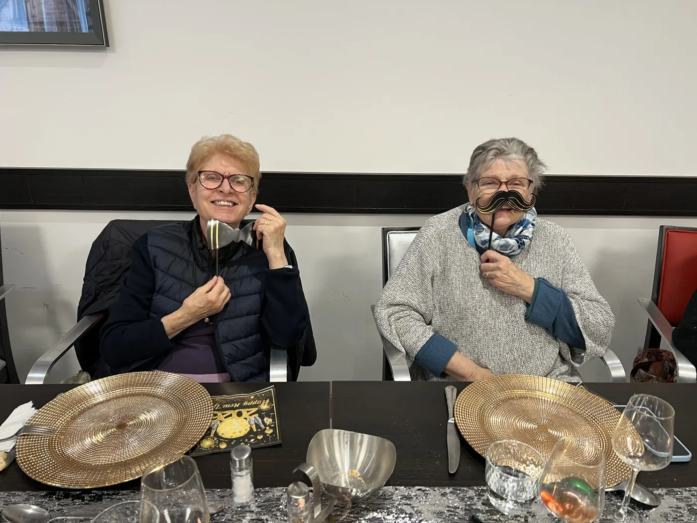 Two residents holding photo-booth props up to their faces at the table