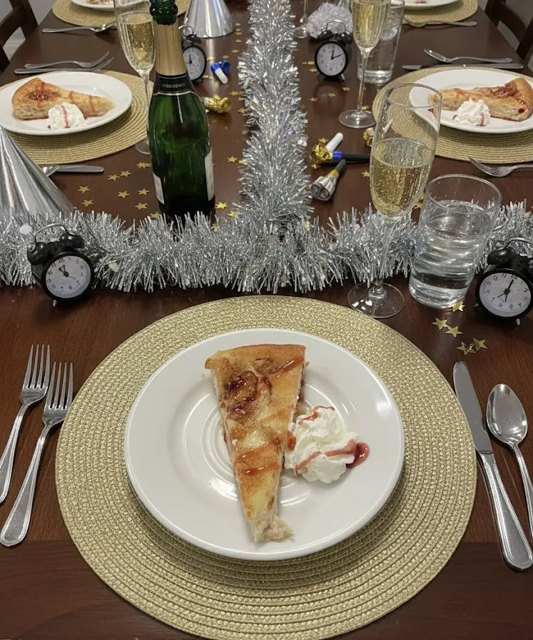 A plate of savoury pie on a New Year table with silver tinsel, clocks and a champagne bottle