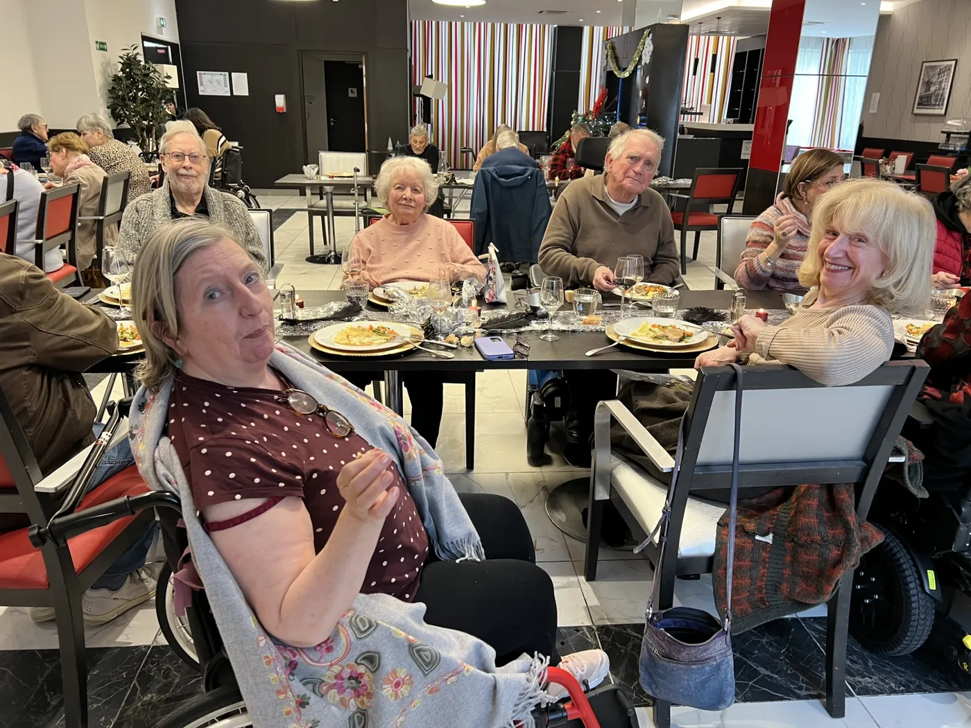Residents seated at round tables in the dining room, one smiling at the camera