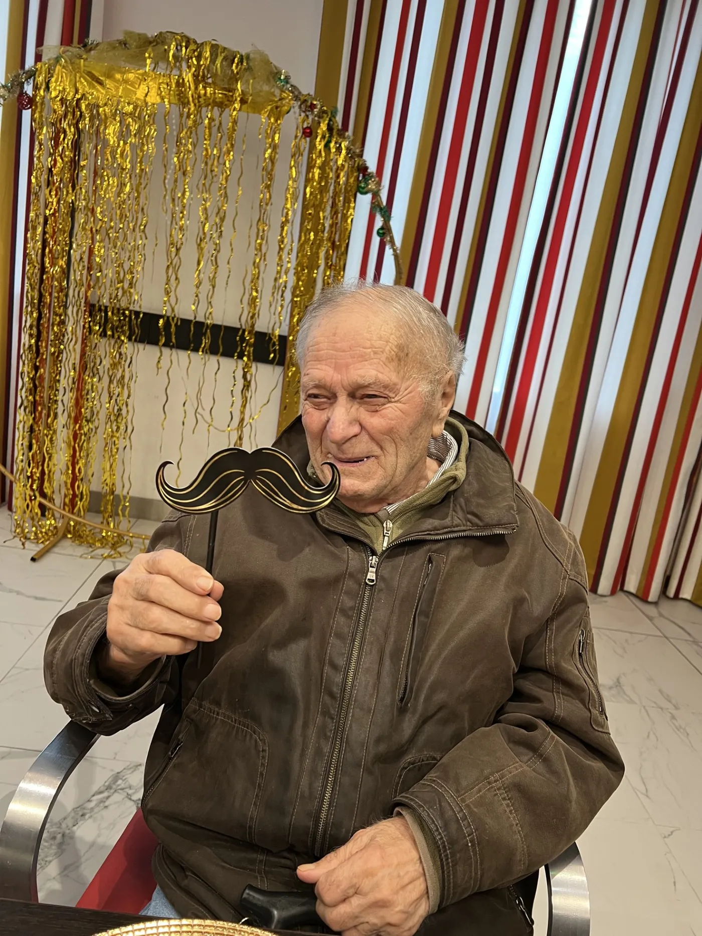A resident posing with a false moustache in front of a gold tinsel backdrop