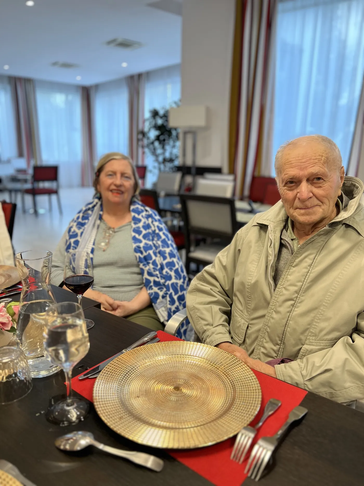 Two residents at a table set with gold chargers, glasses of red wine in front of them