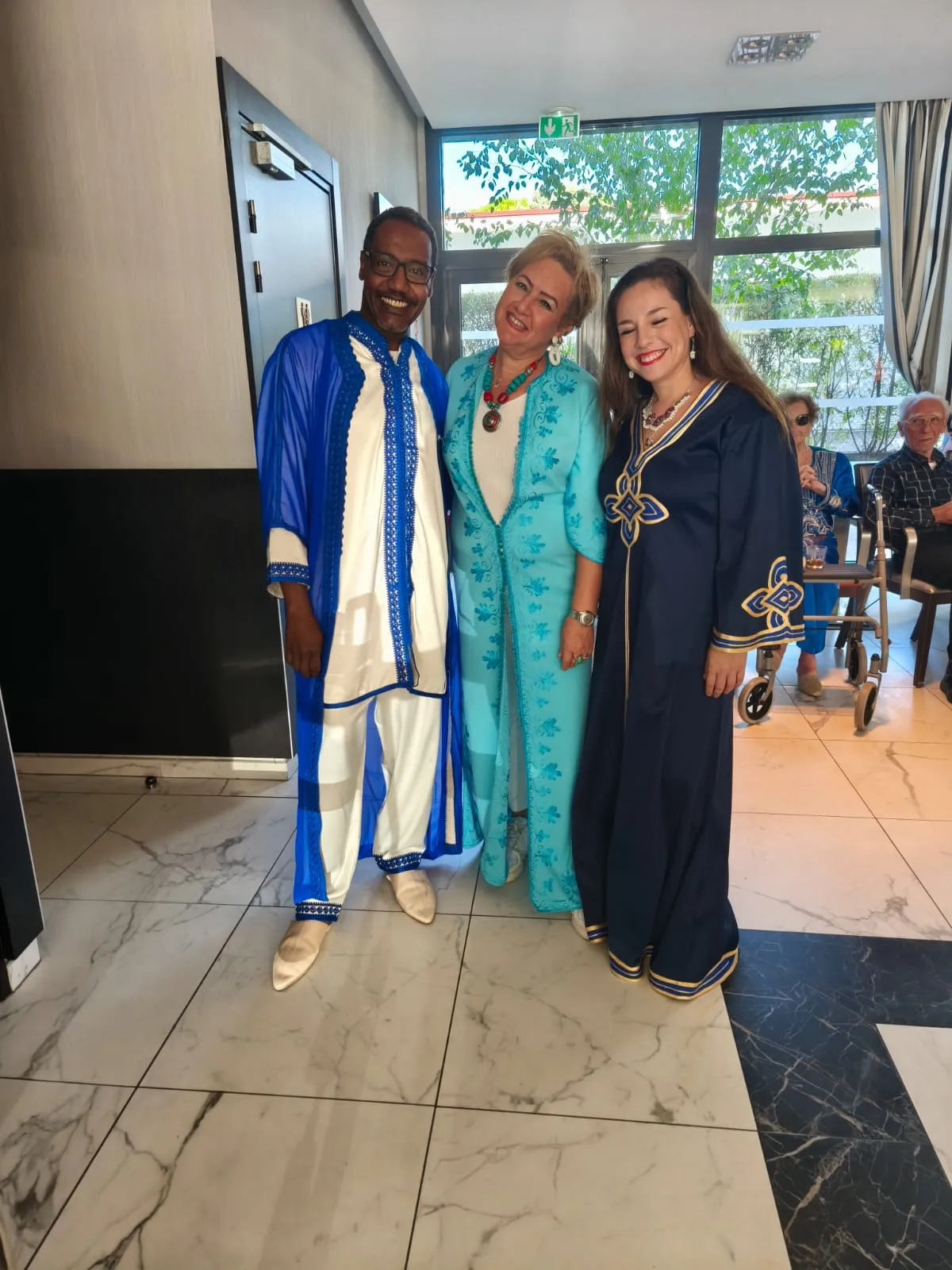 Three performers in blue and turquoise robes posing together in the lounge