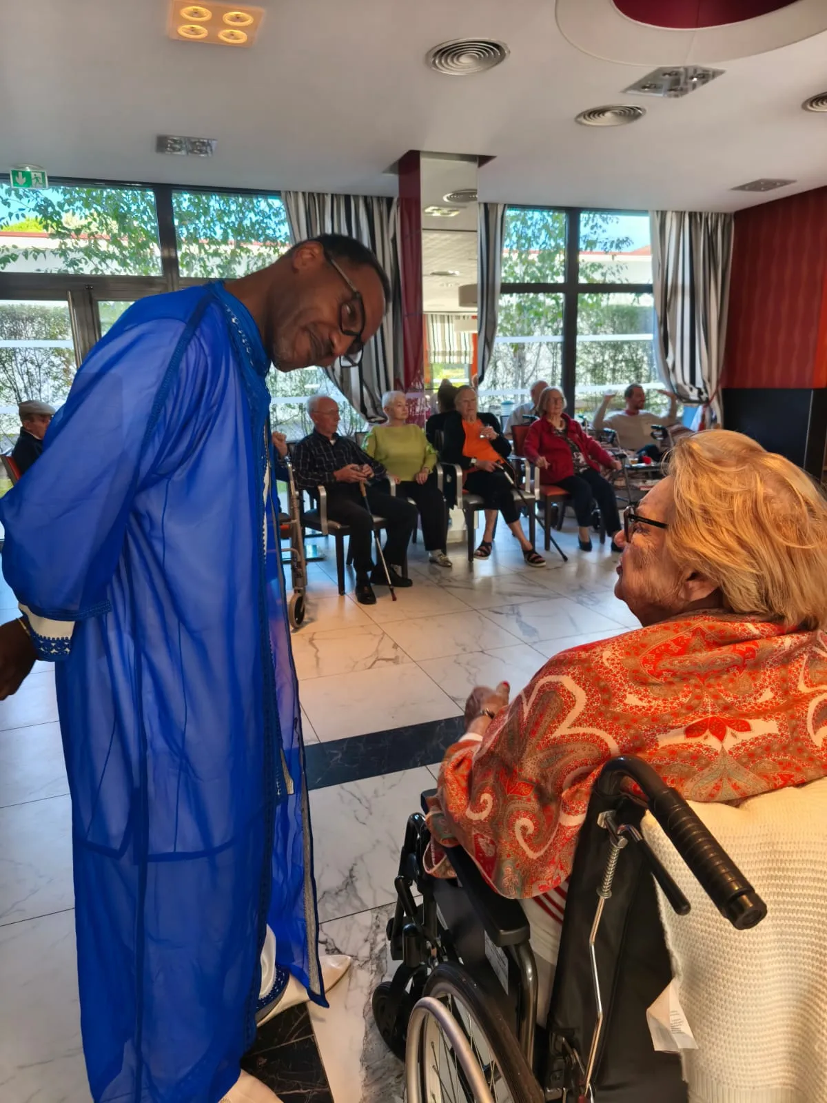 A performer in a blue robe leaning towards a resident in her wheelchair