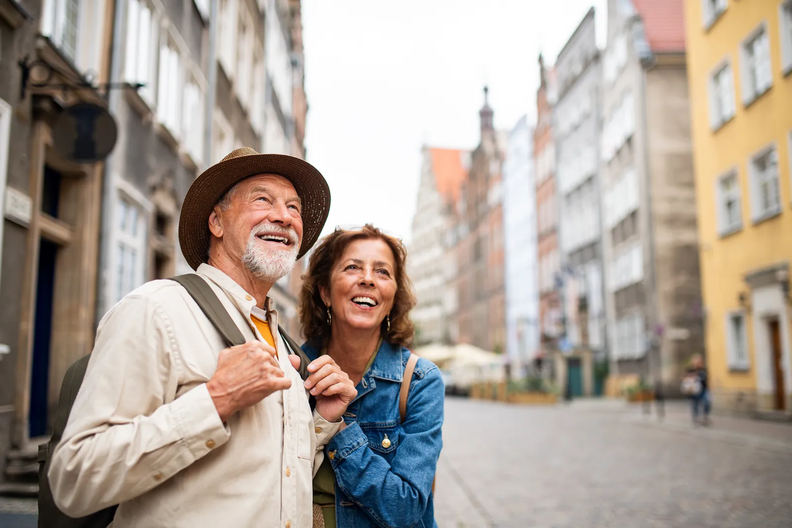 A senior couple walking arm in arm through a colourful old-town street