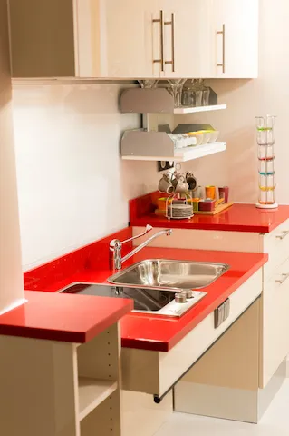 Une kitchenette d'appartement avec plan de travail rouge, évier et meubles à hauteur réglable