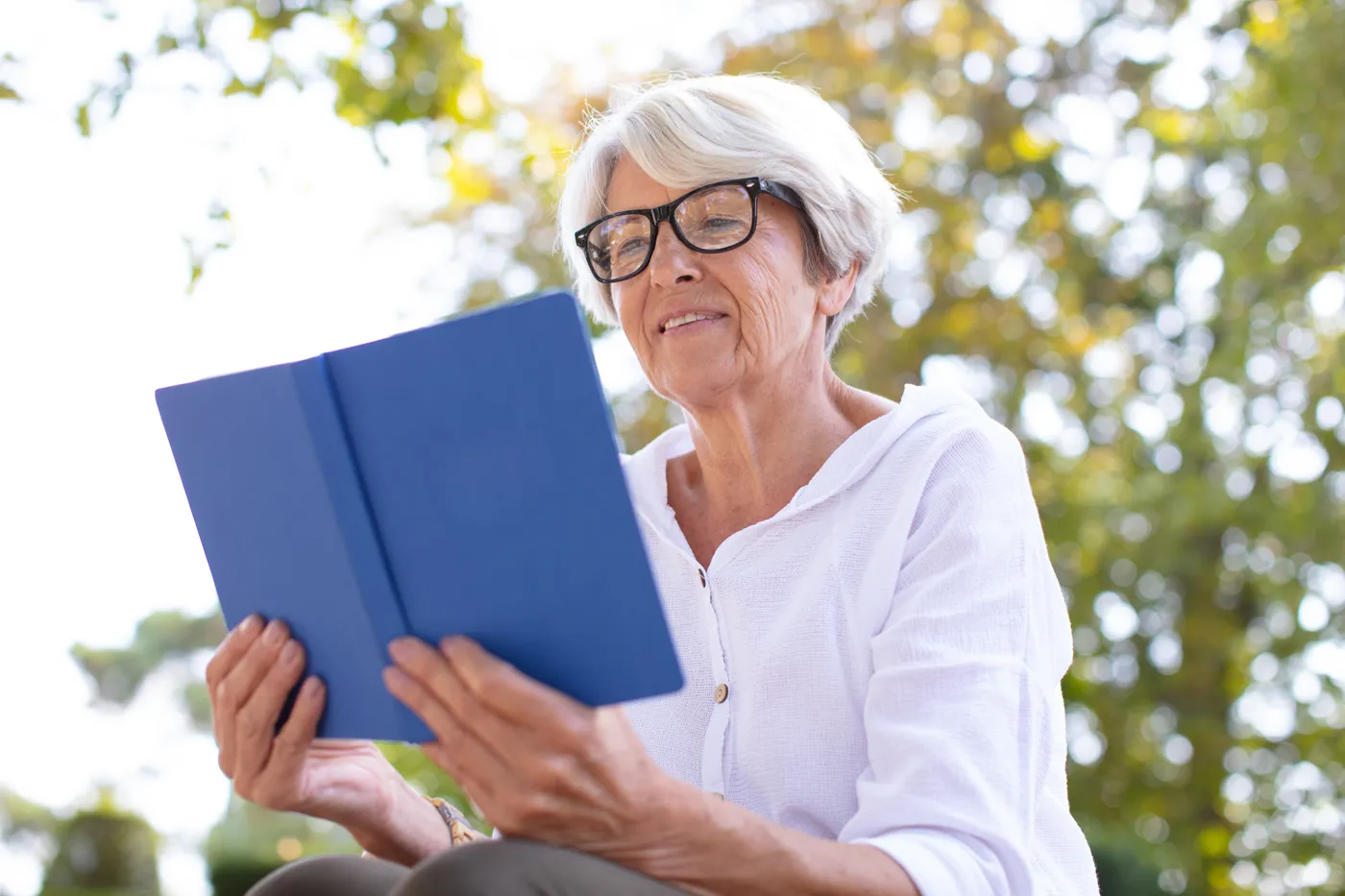 An older woman sitting outside with a blue book open in her hands