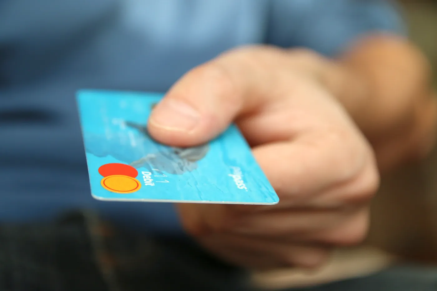 A hand holding out a blue bank card