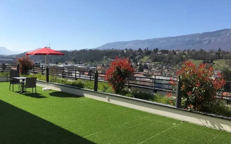 A rooftop terrace with artificial lawn, parasol and a view over the valley to the mountains