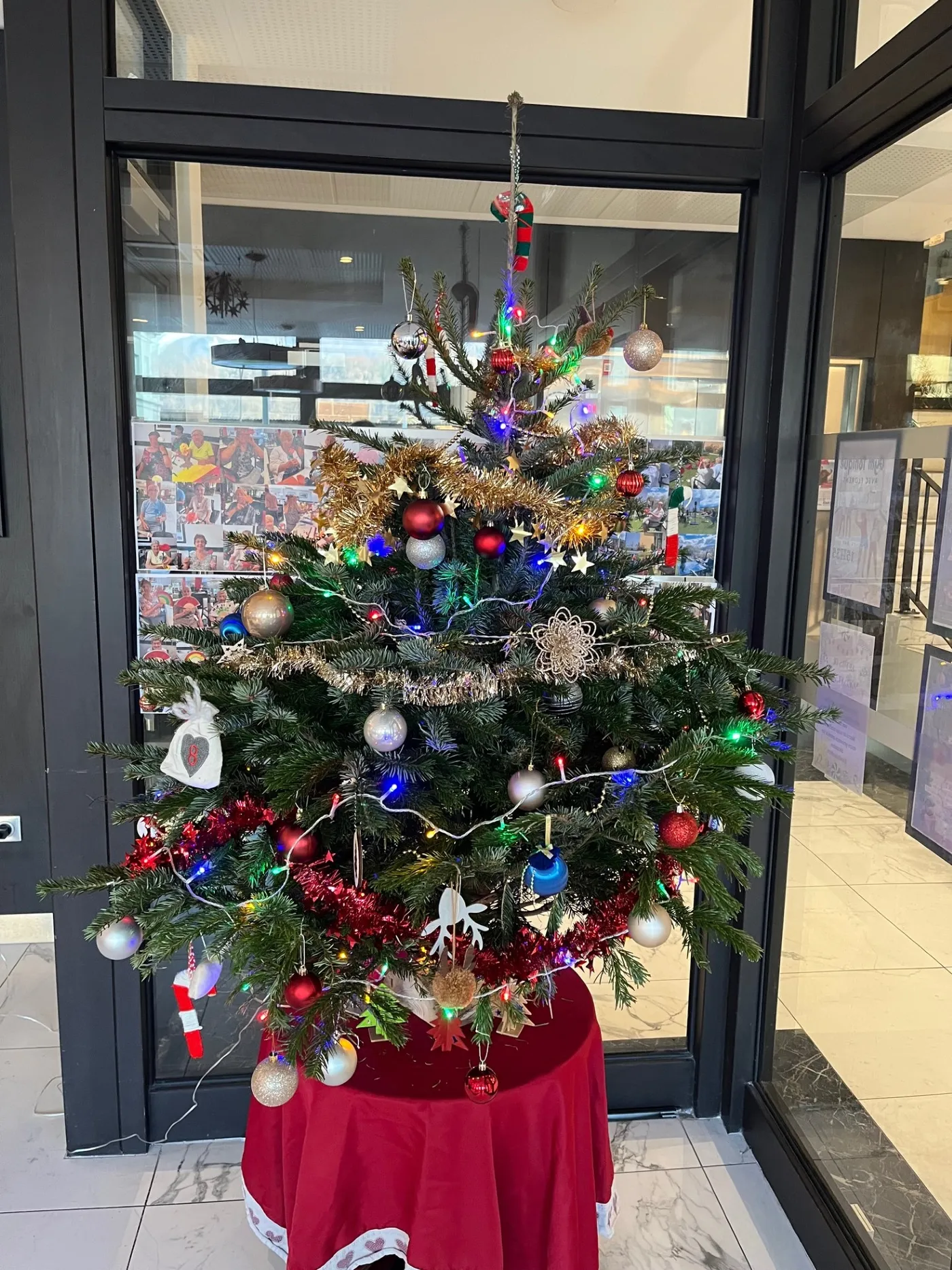 A decorated Christmas tree with baubles and lights standing by the glass door