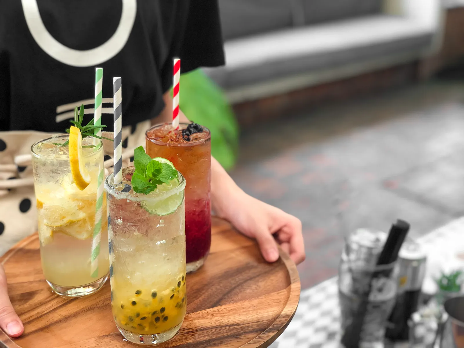Three colourful alcohol-free cocktails with striped straws and fresh fruit, served on a wooden board