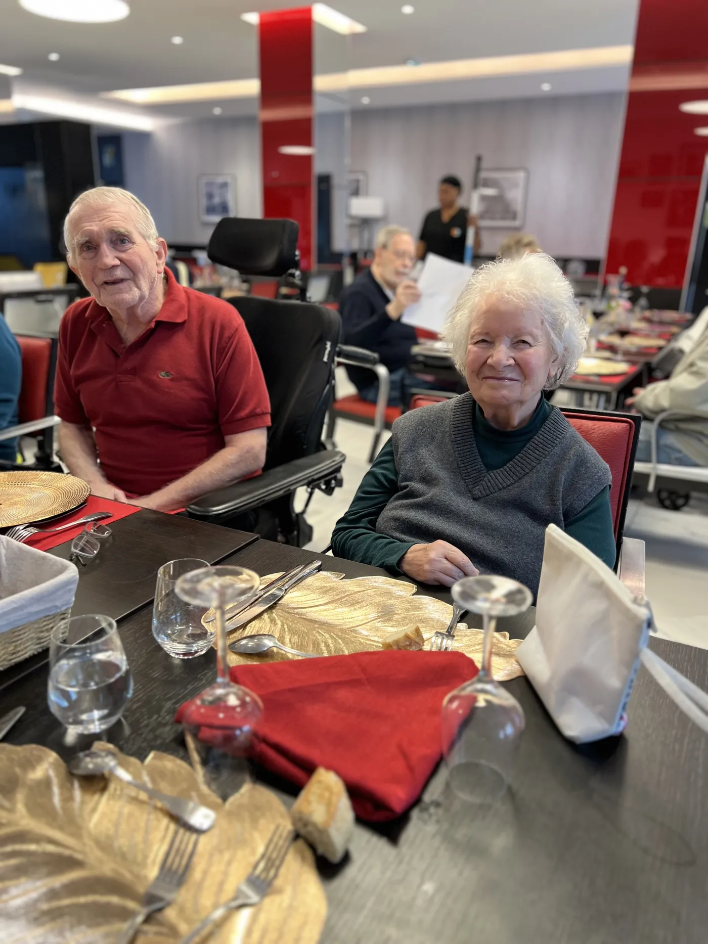 Un résident en polo rouge et sa voisine de table devant leurs couverts