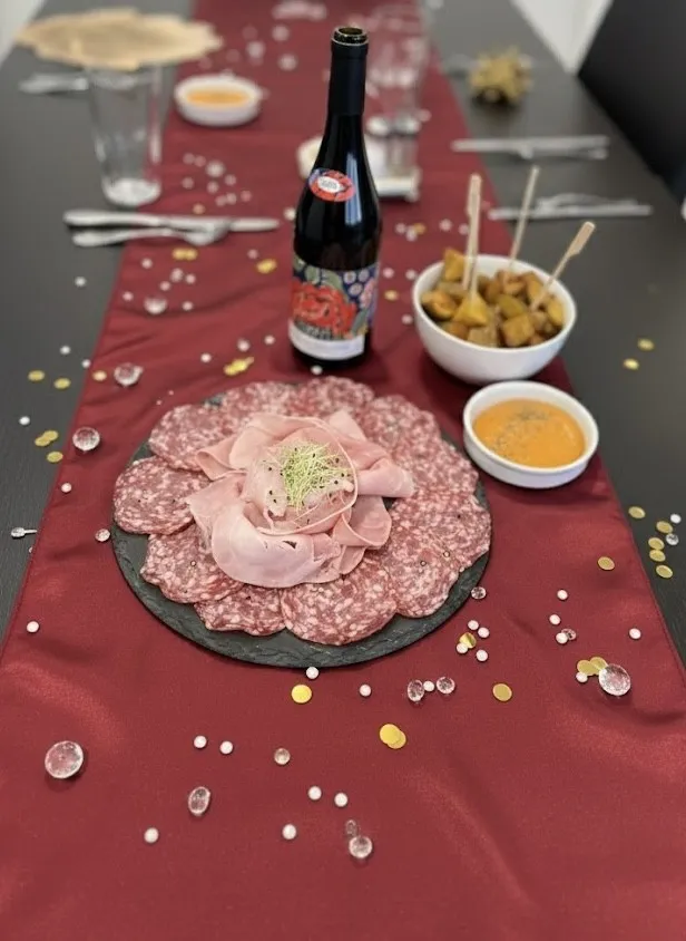 Une ardoise de charcuterie et une bouteille de beaujolais posées sur le chemin de table bordeaux