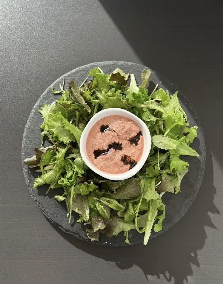 Une salade verte disposée en couronne autour d'un ramequin de rillettes sur une ardoise