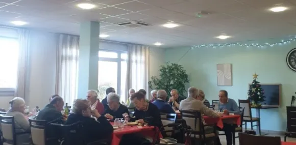 Des résidents déjeunent à leurs tables dans la salle lumineuse, un sapin de Noël dans le coin