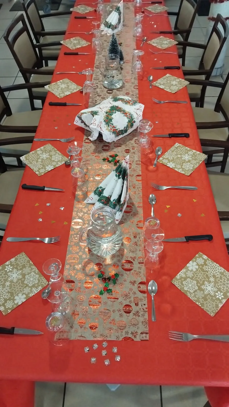 Une longue table dressée d'un chemin de table rouge et de décorations argentées pour le repas de Noël